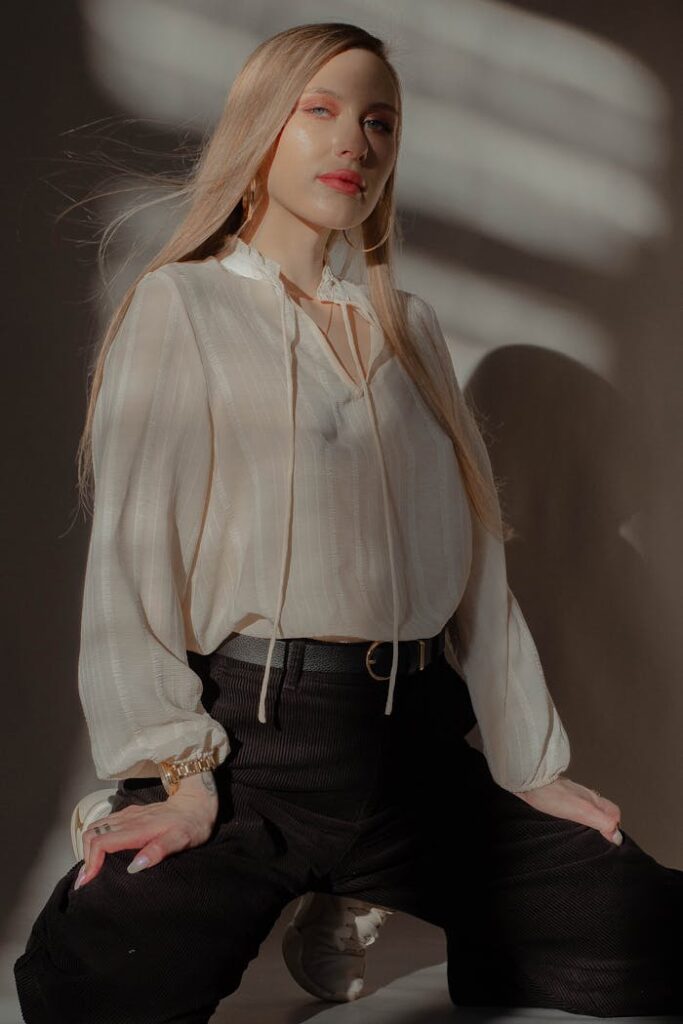 Young stylish woman with flying hair in blouse and trousers looking at camera in sunshine indoors